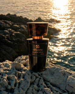 Flacon noir Olfazeta by Chogan Millésime, bouchon écaille, sur rochers clairs face à la mer scintillante