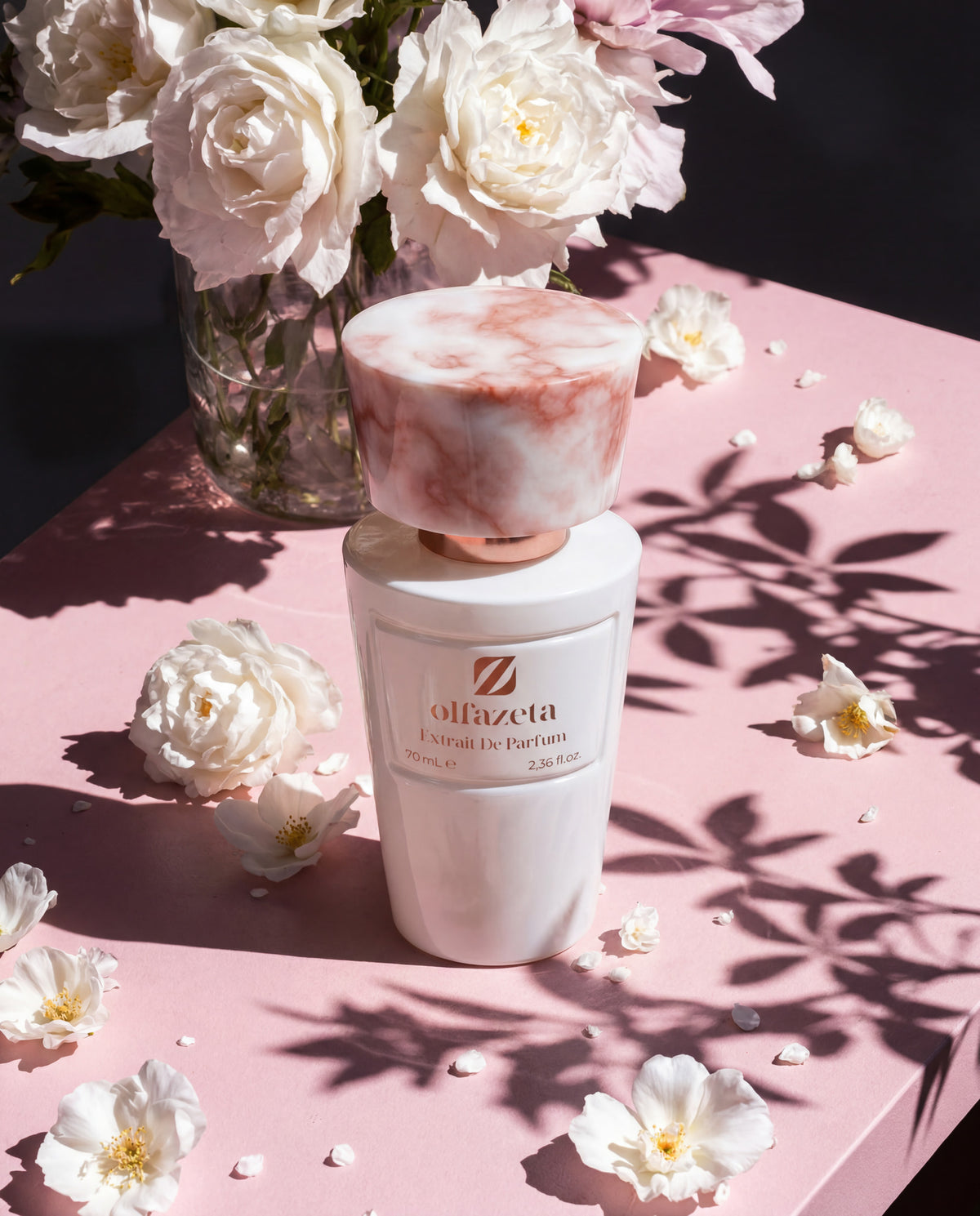 Flacon blanc Olfazeta by Chogan Millésime N°51 entouré de roses blanches, ombres de feuillage au soleil
