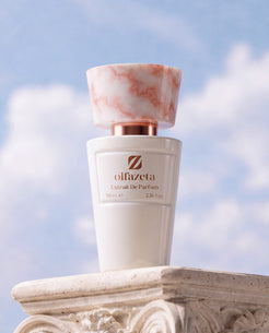 Flacon blanc Olfazeta by Chogan Millésime N°06 sur un chapiteau de colonne sculpté, ciel bleu nuageux